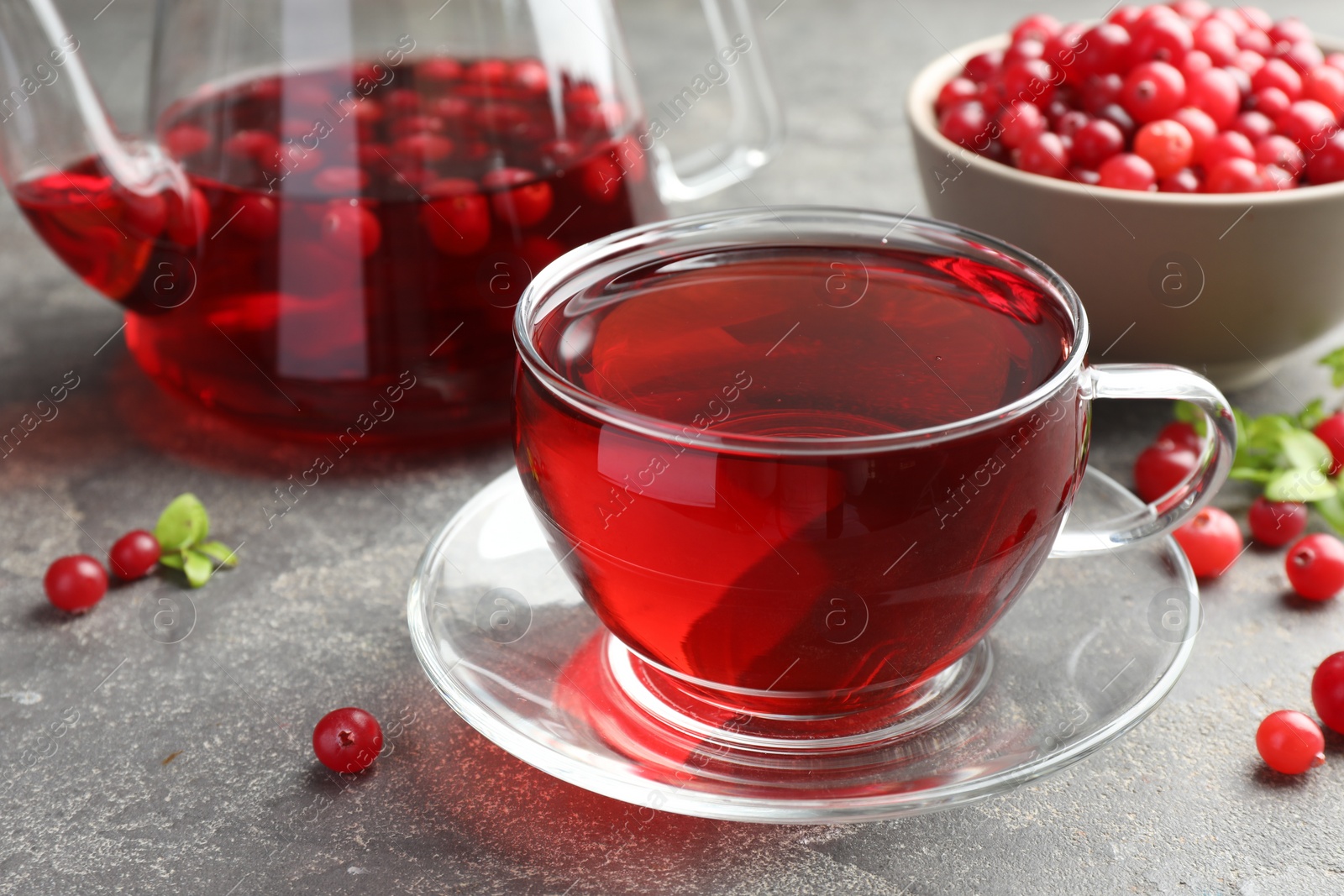 Photo of Tasty hot cranberry tea in glass cup and fresh berries on light grey textured table