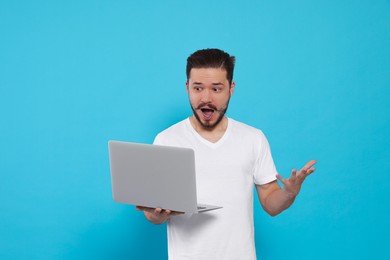 Emotional man looking at laptop on light blue background