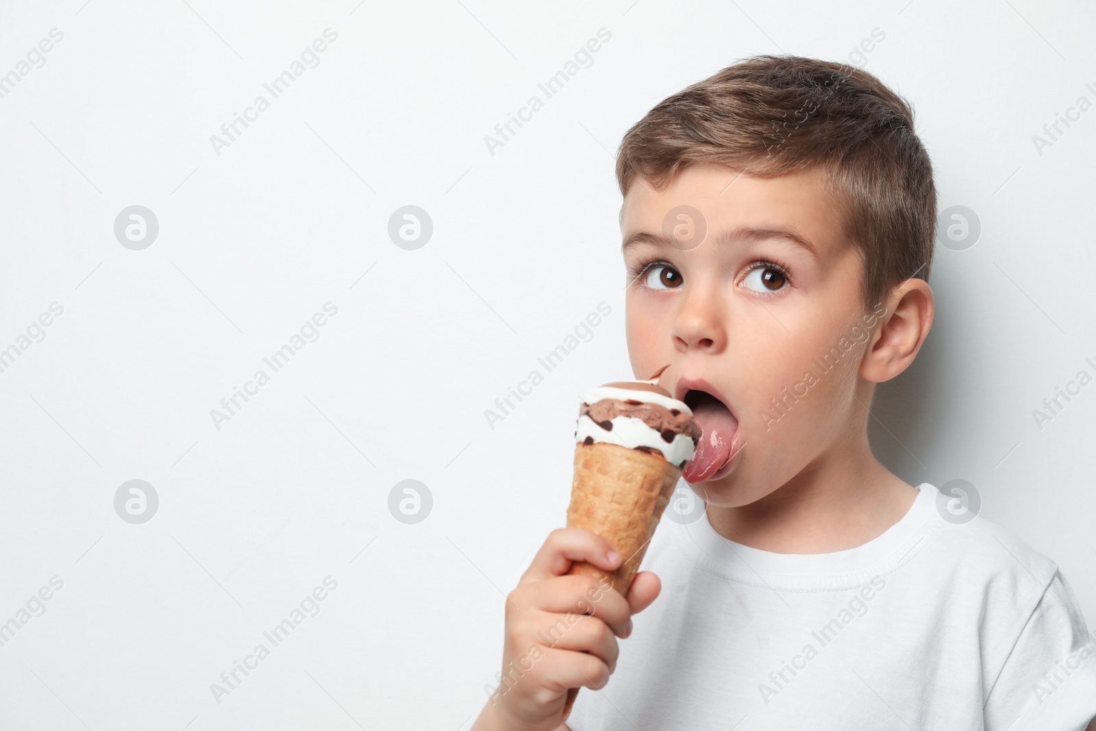 Photo of Adorable little boy with delicious ice cream against light background