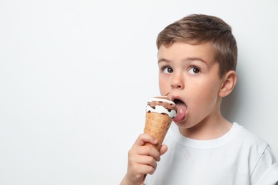 Adorable little boy with delicious ice cream against light background