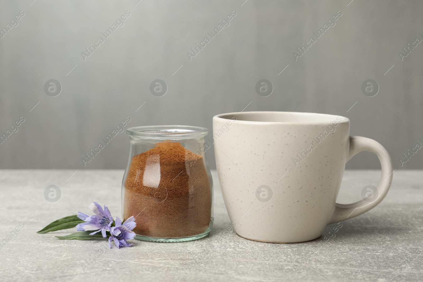 Photo of Jar with chicory powder, cup and flowers on light grey table
