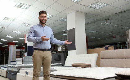 Young salesman showing modern orthopedic mattress in store