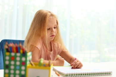 Photo of Cute little left-handed girl drawing at table in room