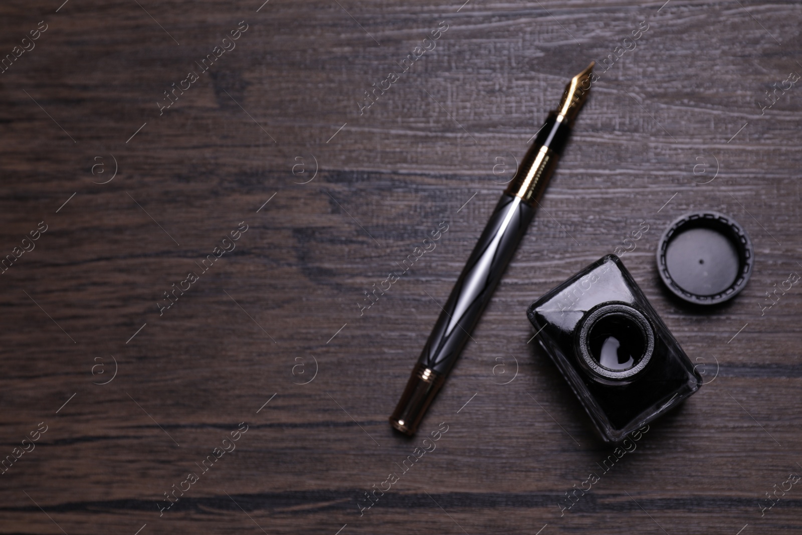 Photo of Inkwell and fountain pen on wooden table, flat lay. Space for text