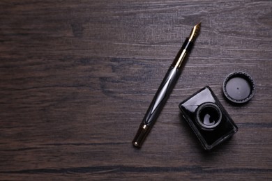 Photo of Inkwell and fountain pen on wooden table, flat lay. Space for text