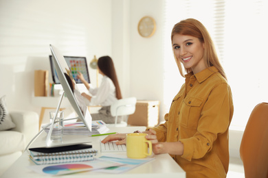 Portrait of happy female designer at table in office