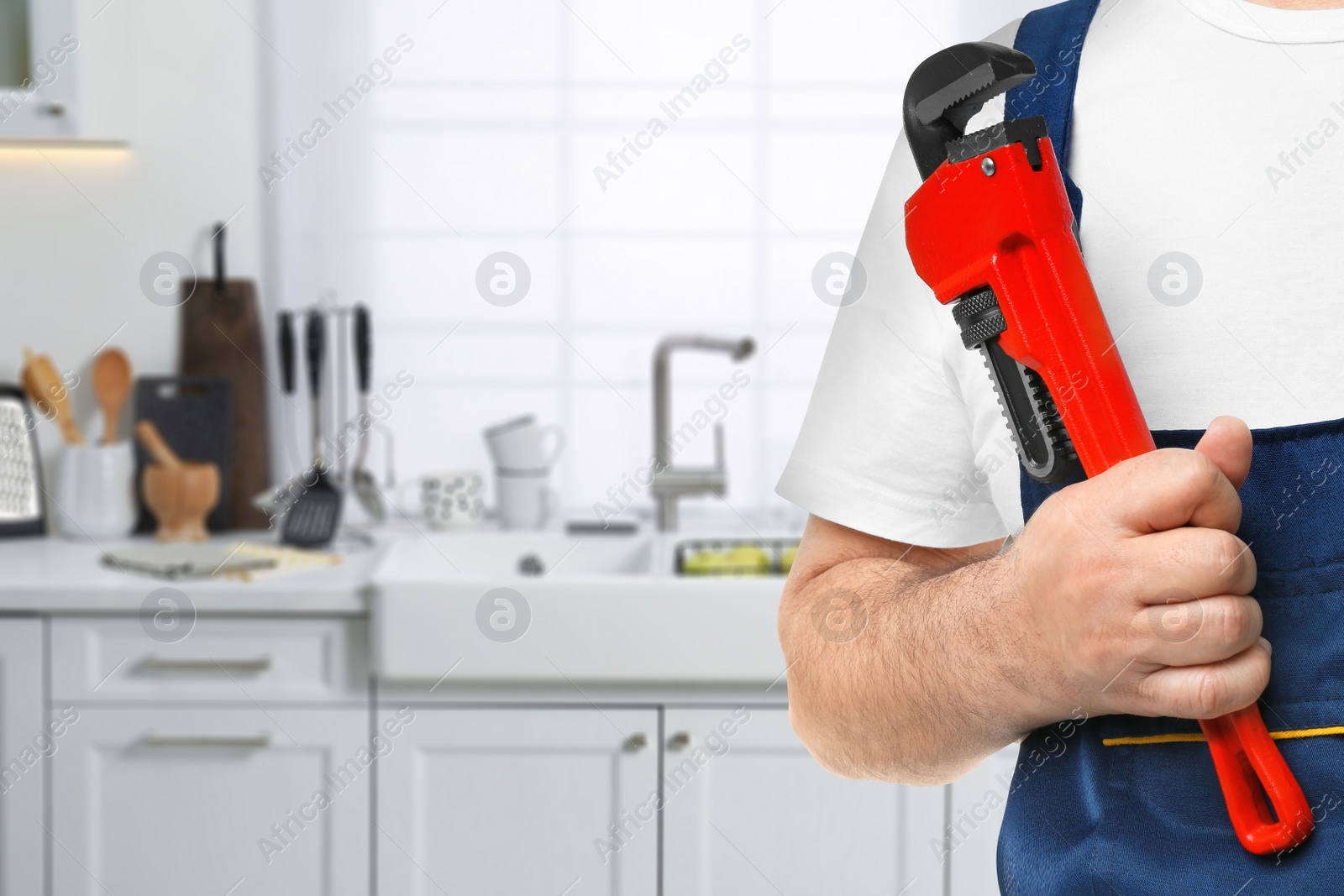 Image of Plumber with pipe wrench in kitchen, closeup. Space for text