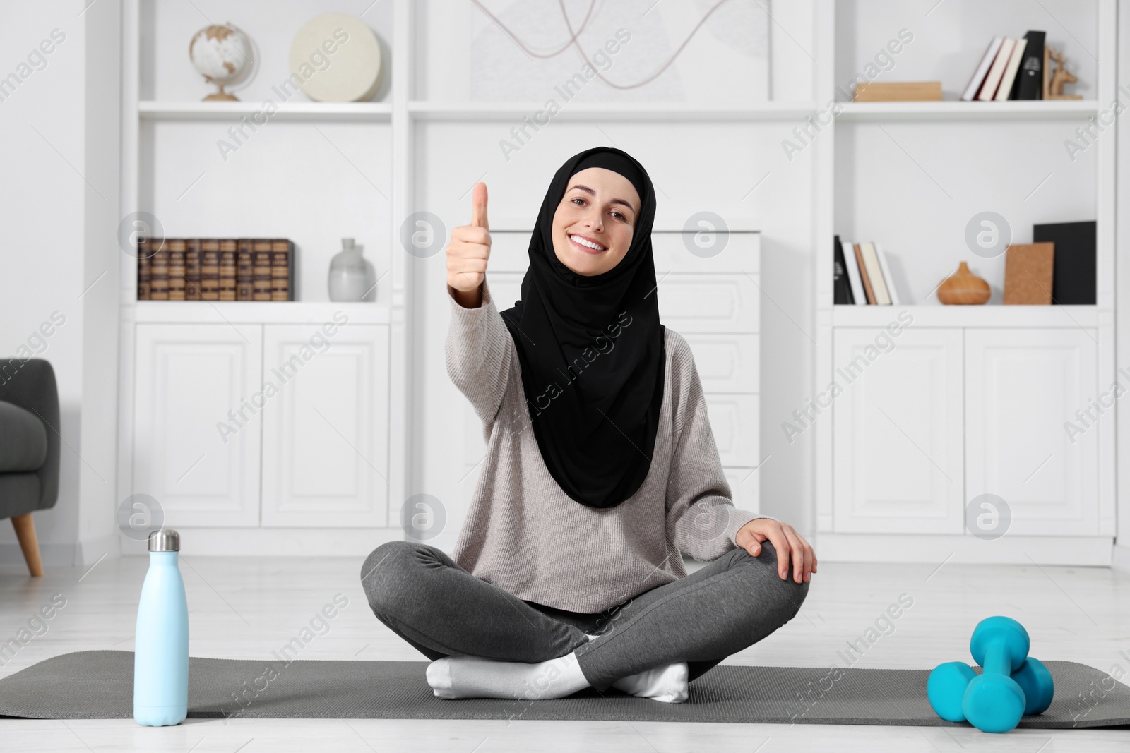 Photo of Muslim woman showing thumb up on fitness mat at home