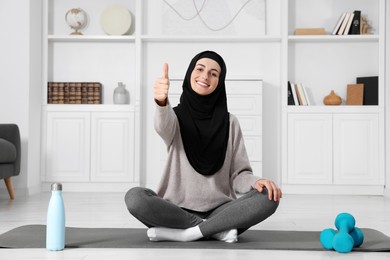 Photo of Muslim woman showing thumb up on fitness mat at home