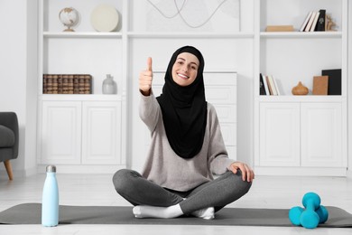 Muslim woman showing thumb up on fitness mat at home