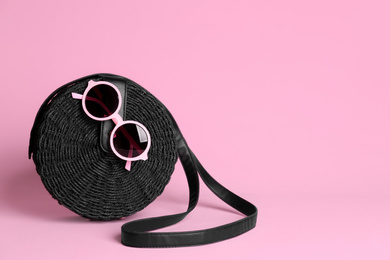 Photo of Stylish woman's bag and sunglasses on light pink background. Space for text