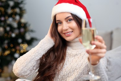 Beautiful young smiling woman in Santa hat with glass of sparkling wine at home