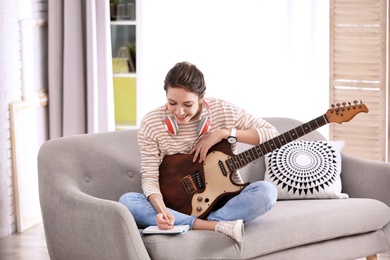 Photo of Young woman with electric guitar composing song in living room