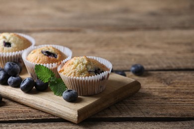 Photo of Delicious sweet muffins with blueberries and mint on wooden table, closeup. Space for text