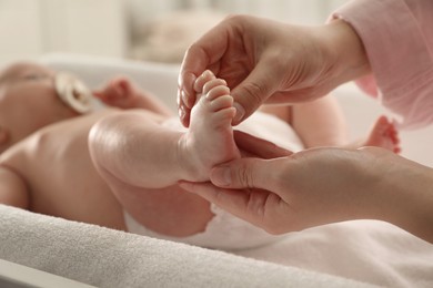 Photo of Mother massaging her cute baby with oil on changing table, closeup