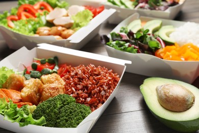 Photo of Different healthy meals in takeaway boxes on wooden table, closeup. Food delivery