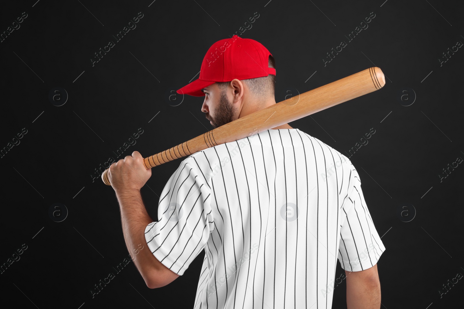 Photo of Man in stylish red baseball cap holding bat on black background, back view