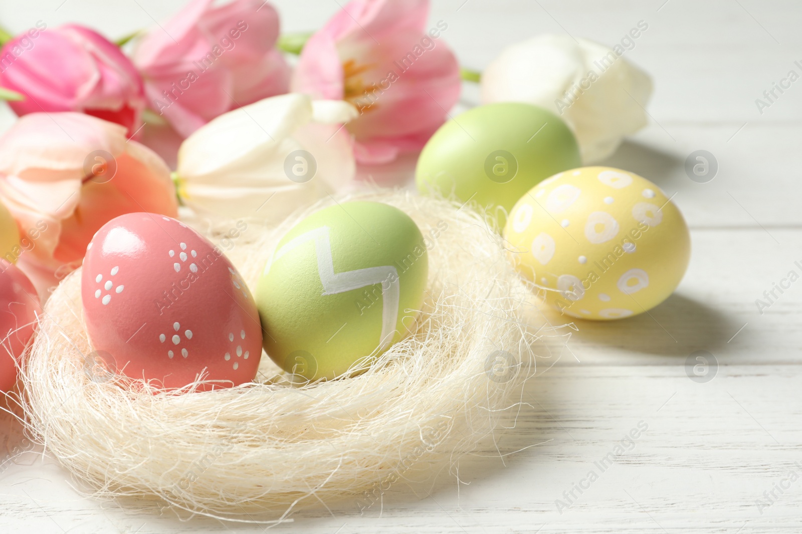 Photo of Sisal nest and painted Easter eggs on wooden table, space for text