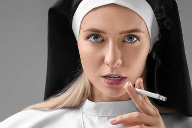 Photo of Woman in nun habit smoking cigarette on grey background, closeup