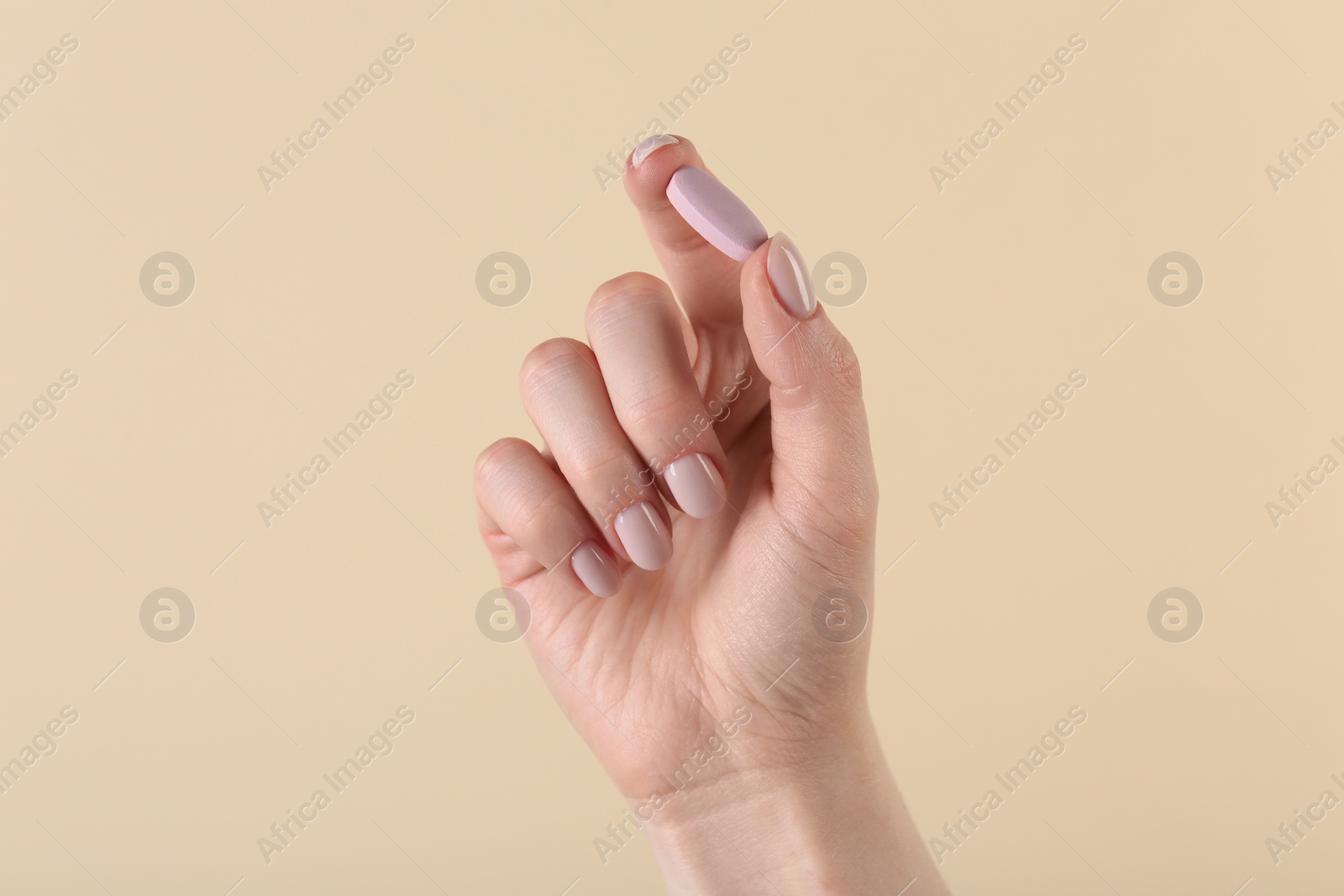 Photo of Woman holding vitamin pill on beige background, closeup. Health supplement