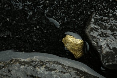 Photo of Shiny gold nugget on wet stones, top view