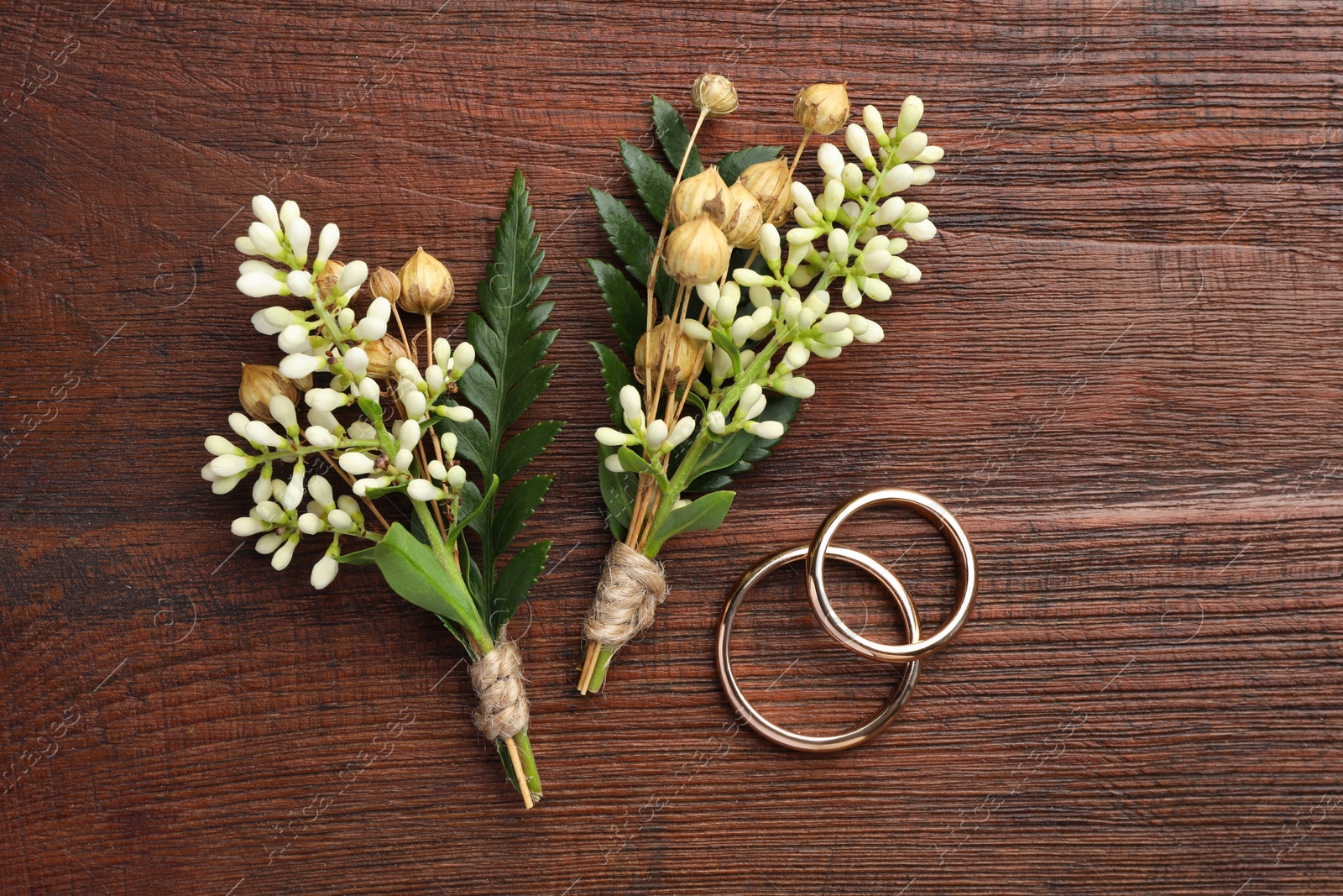 Photo of Small stylish boutonnieres and rings on wooden table, flat lay