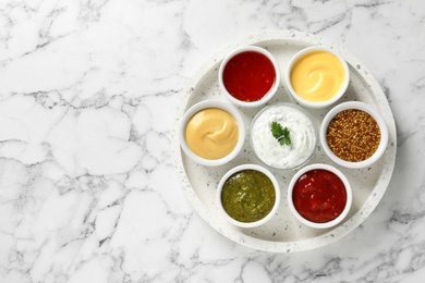 Set of different delicious sauces on white marble table, top view. Space for text