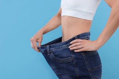 Photo of Slim woman wearing big jeans on light blue background, closeup. Weight loss