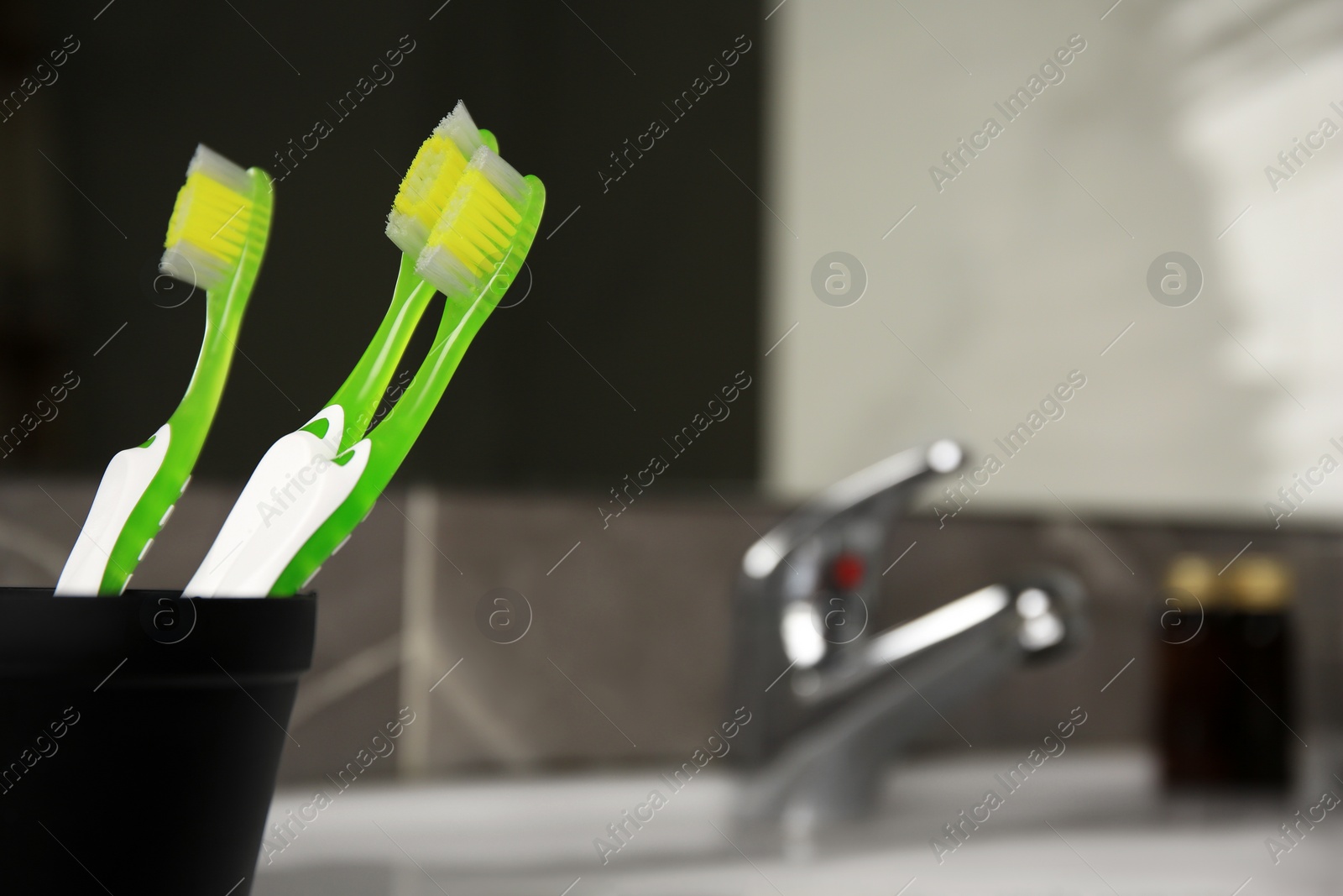 Photo of Light green toothbrushes in black toothbrush holder indoors, space for text