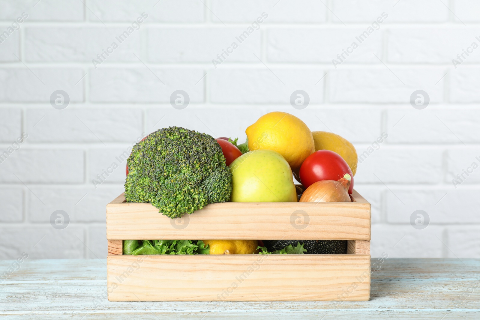 Photo of Wooden crate with fruits and vegetables on table near white brick wall, space for text