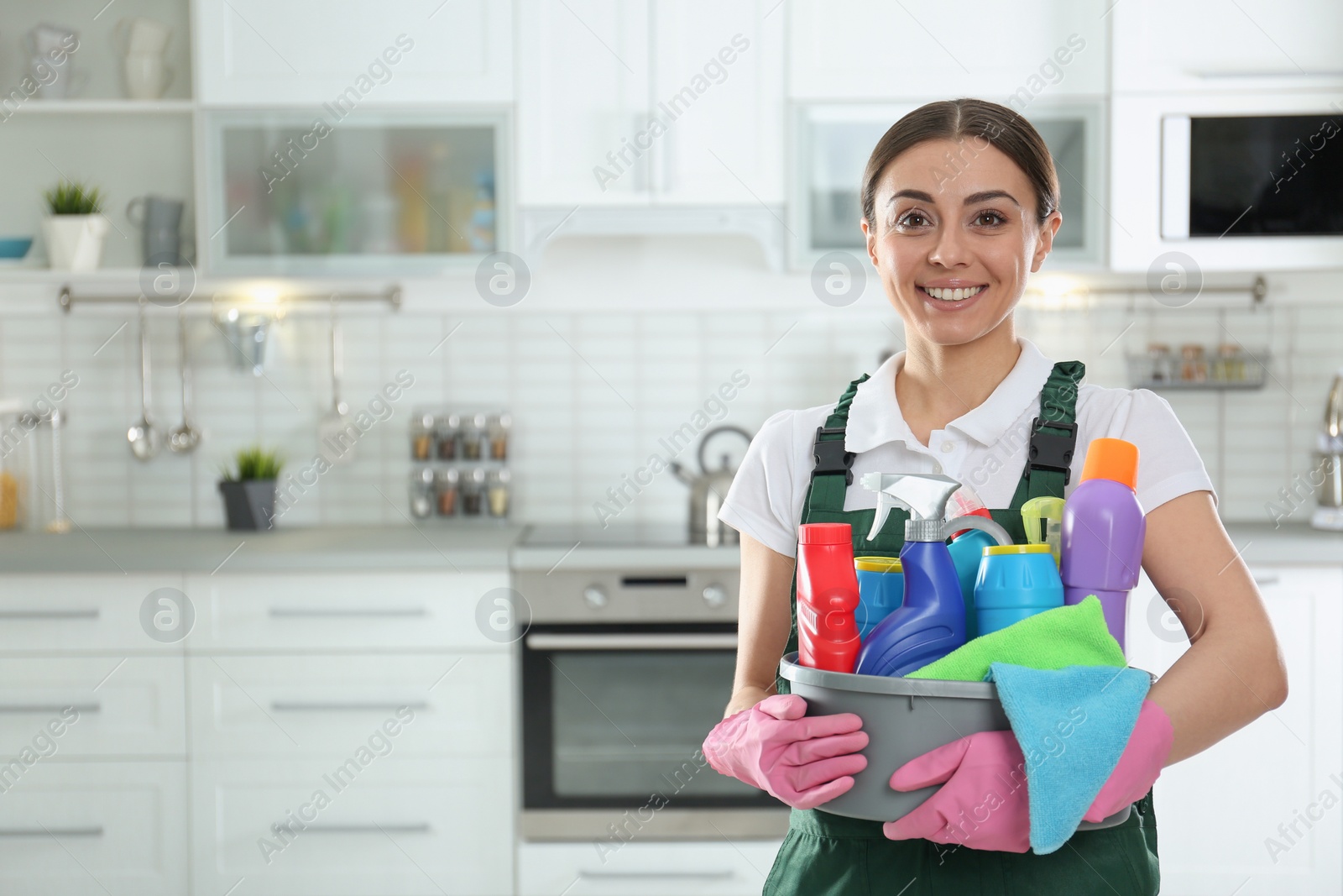 Photo of Portrait of young woman with basin of detergents in kitchen. Cleaning service