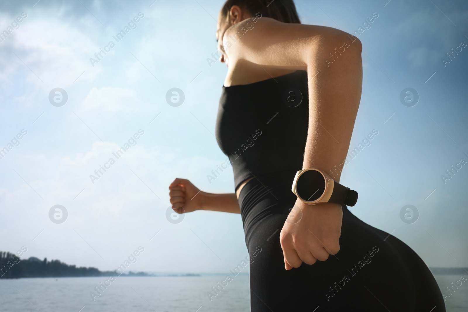 Photo of Woman wearing modern smart watch during training near river, focus on hand