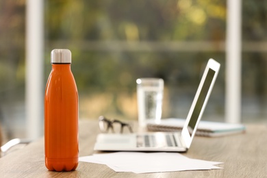 Photo of Modern orange thermos bottle on table in office. Space for text