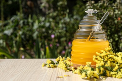 Photo of Delicious fresh honey and beautiful flowers on wooden table in garden, space for text
