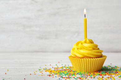 Delicious birthday cupcake with cream and burning candle on white wooden table. Space for text