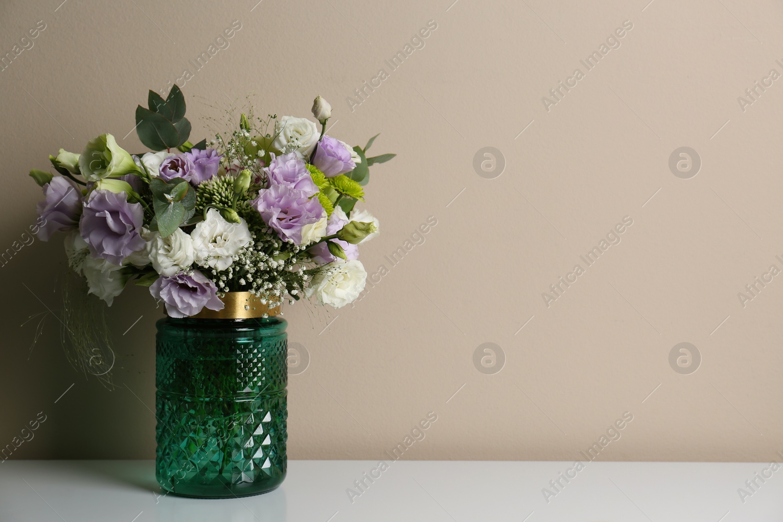 Photo of Bouquet with beautiful Eustoma flowers in vase on white table against beige background. Space for text
