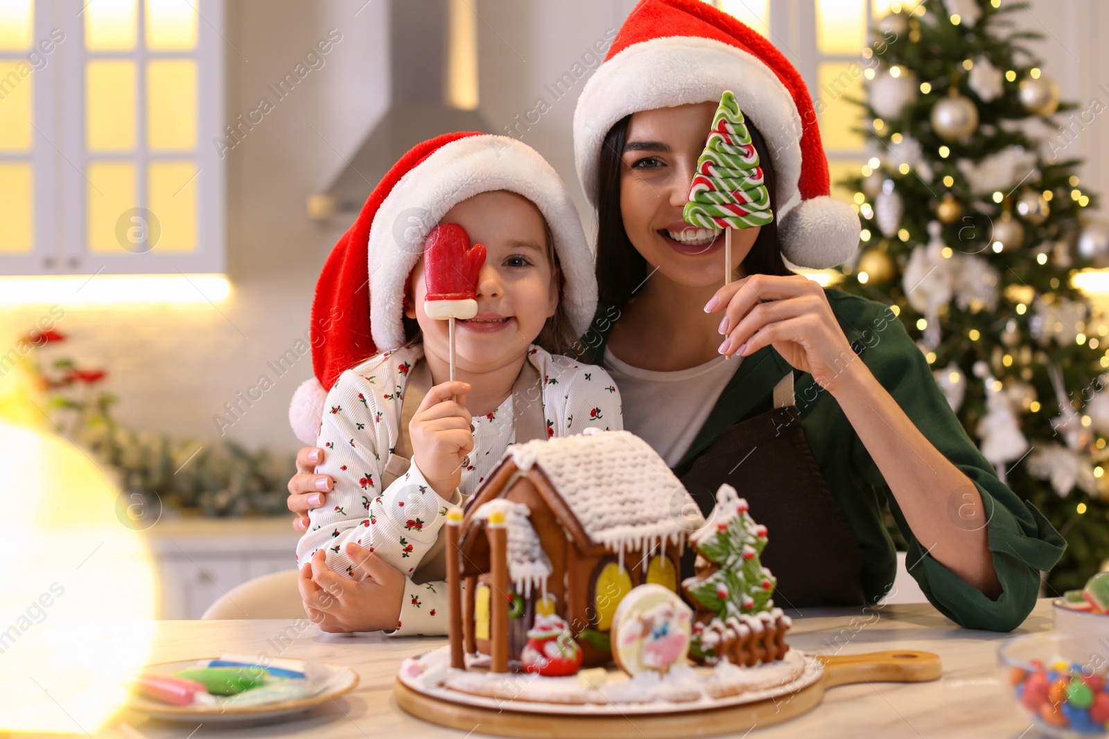 Photo of Mother and daughter having fun while decorating gingerbread house at table indoors