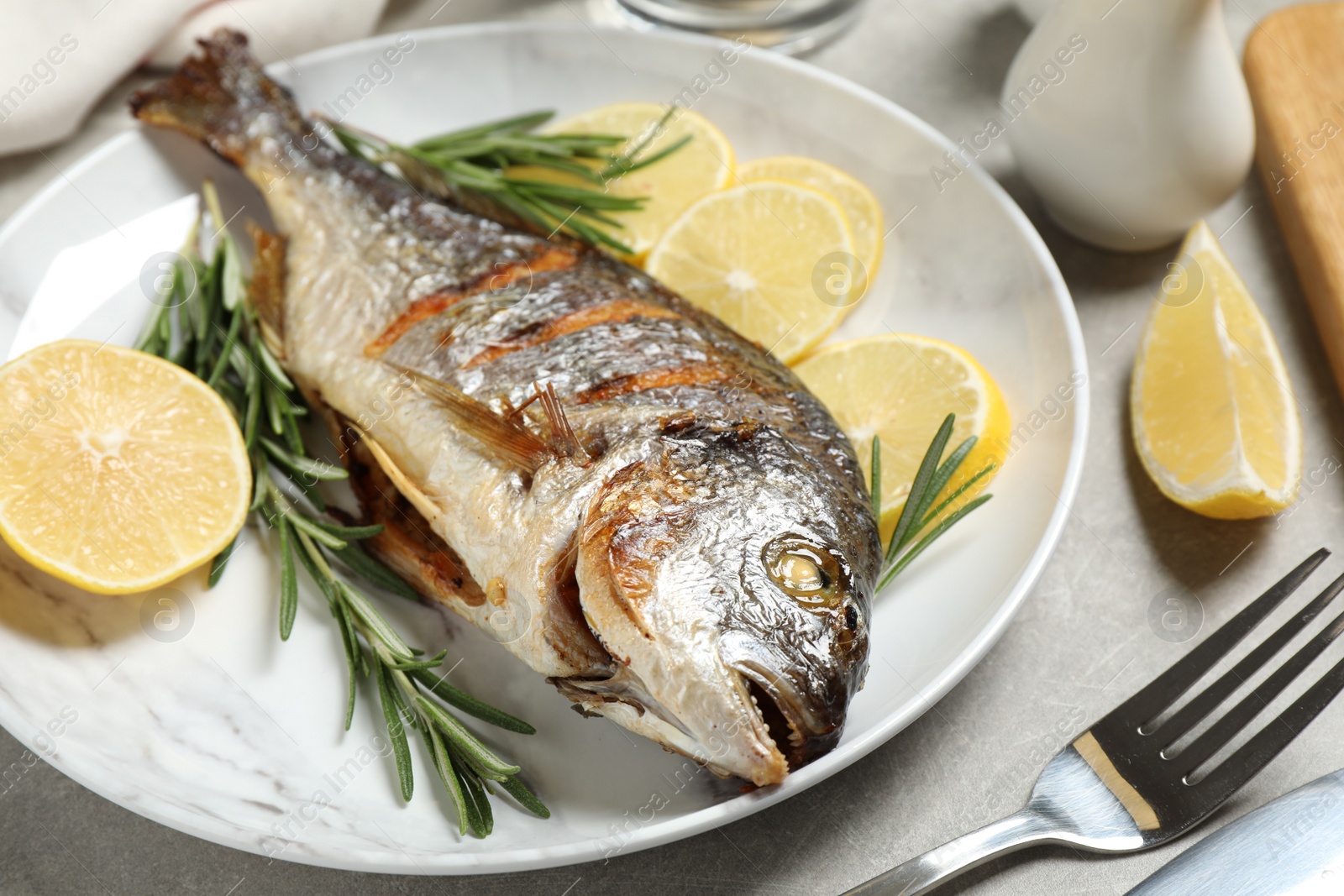 Photo of Delicious roasted fish with lemon on grey table, closeup