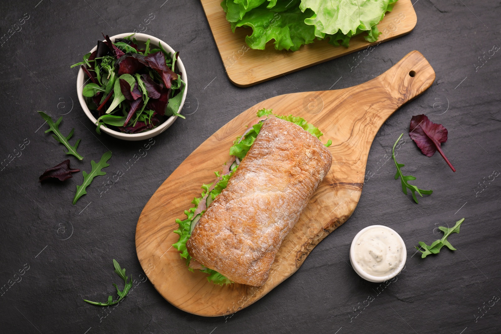 Photo of Delicious sandwich with salmon and ingredients on black table, flat lay