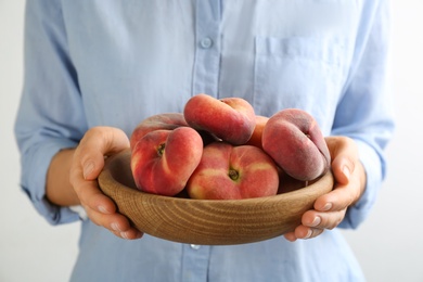 Photo of Woman holding bowl of fresh ripe donut peaches on light background, closeup