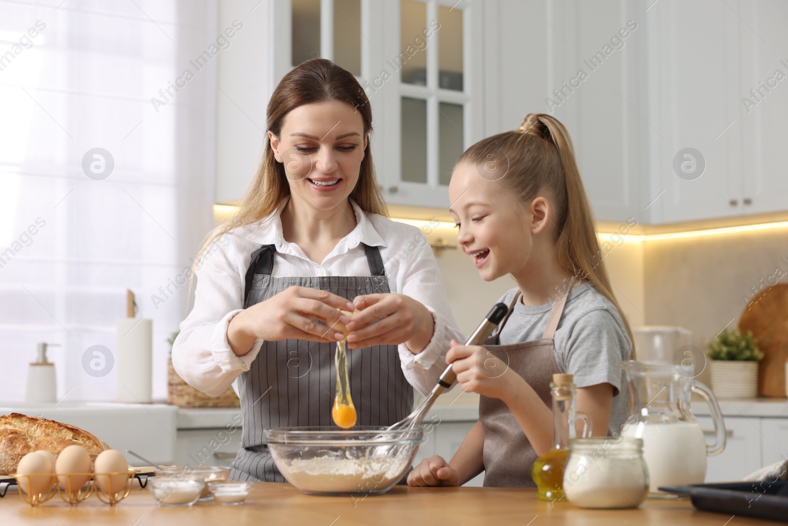 Photo of Making bread. Mother and her daughter preparing dough at wooden table in kitchen