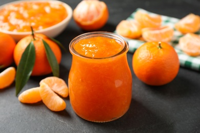 Tasty tangerine jam in glass jar on dark table