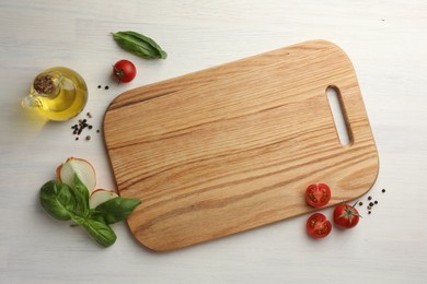 Photo of Cutting board, basil, onion, oil and tomatoes on white wooden table, flat lay. Space for text