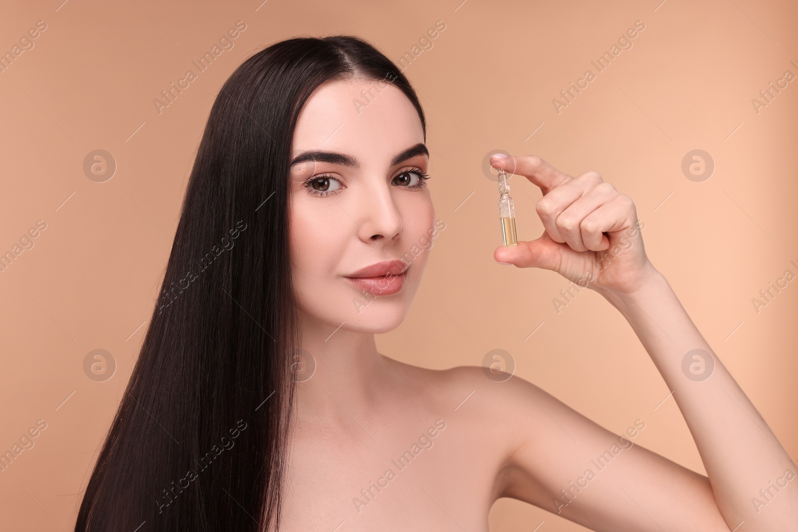 Photo of Beautiful young woman holding skincare ampoule on beige background