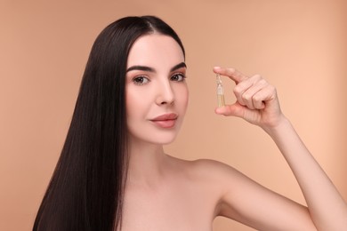 Photo of Beautiful young woman holding skincare ampoule on beige background