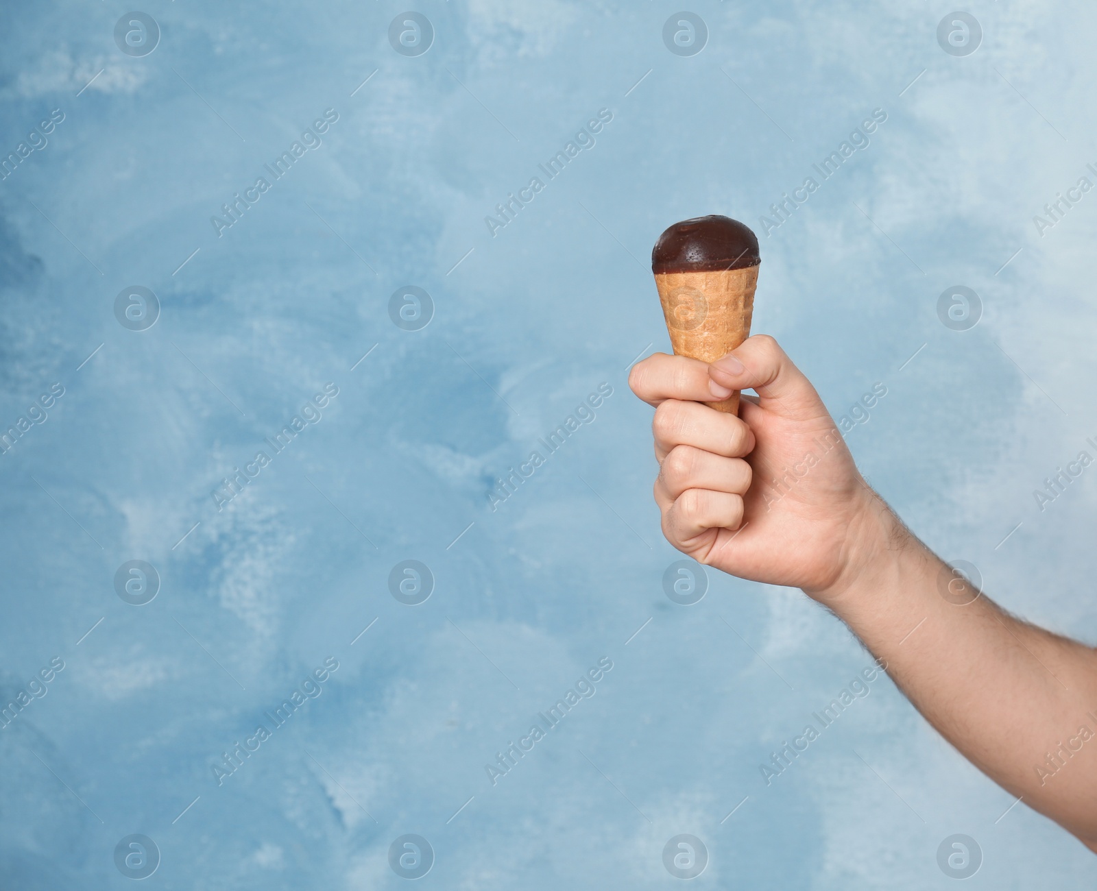 Photo of Man holding yummy ice cream on color background. Focus on hand