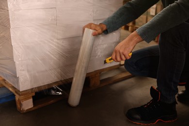 Worker wrapping boxes in stretch film at warehouse, closeup