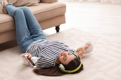 Photo of Young woman with headphones listening to music on floor in living room