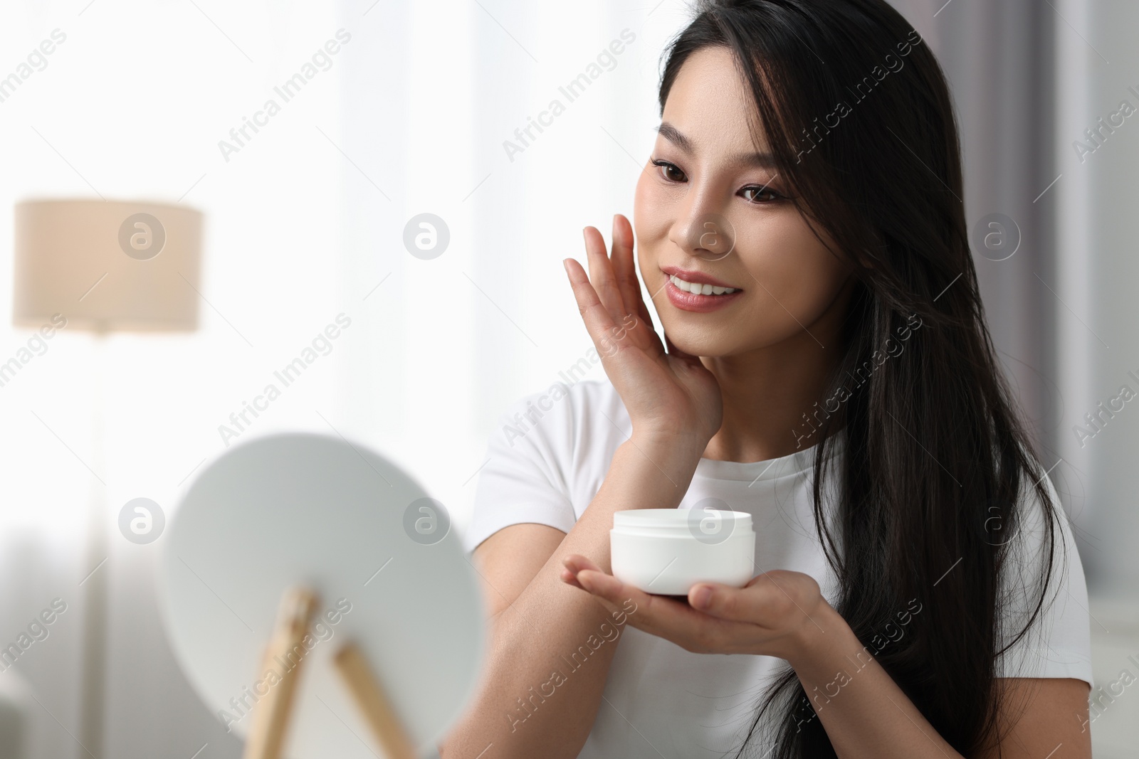 Photo of Happy woman applying face cream at home, space for text