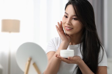 Happy woman applying face cream at home, space for text